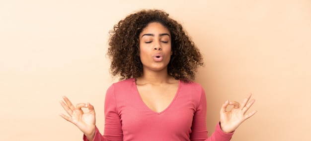 Jeune femme afro-américaine sur mur beige dans une pose zen