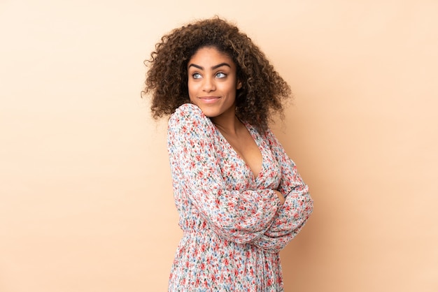 Jeune femme afro-américaine sur mur beige faisant des doutes geste tout en soulevant les épaules