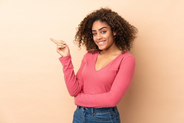 Jeune femme afro-américaine sur le mur beige, pointant le doigt sur le côté