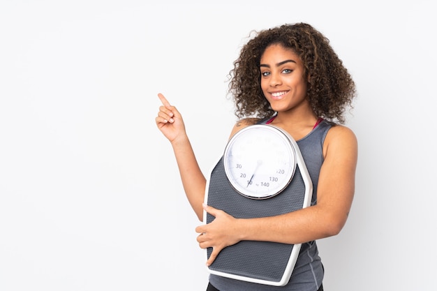 Jeune femme afro-américaine sur mur blanc avec machine de pesage et côté pointage