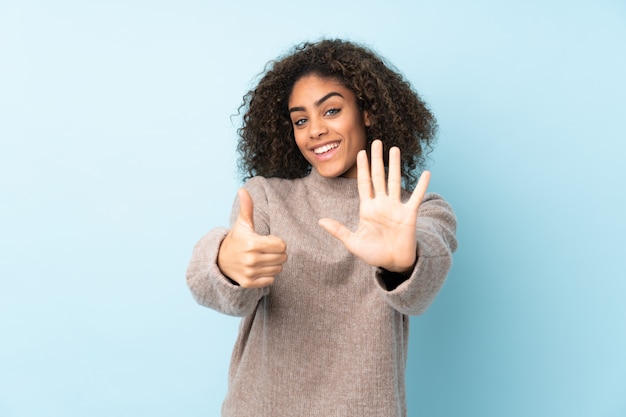 Jeune femme afro-américaine sur mur bleu comptant six avec les doigts