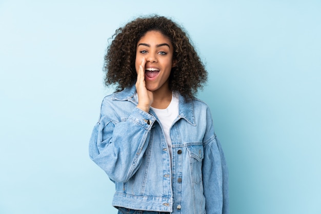 Jeune femme afro-américaine sur mur bleu criant avec la bouche grande ouverte