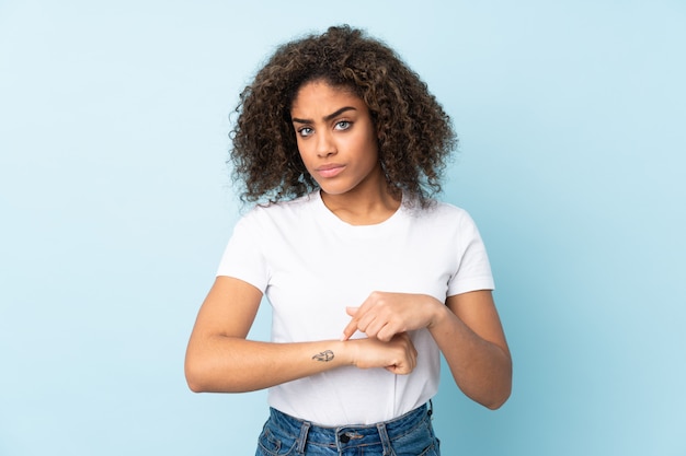 Jeune femme afro-américaine sur le mur bleu faisant le geste d'être en retard