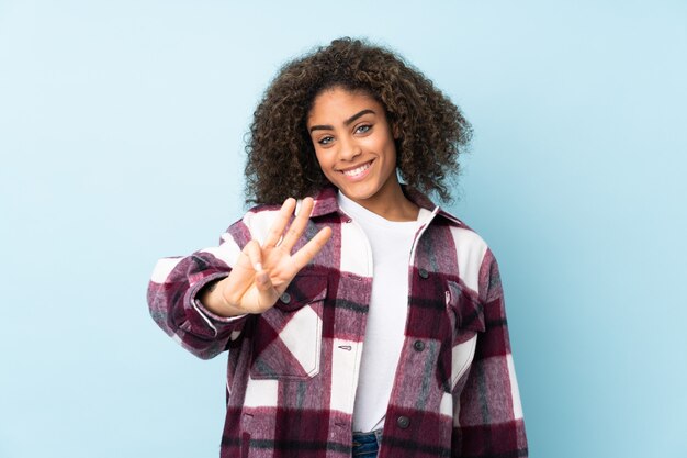 Jeune femme afro-américaine sur mur bleu heureux et en comptant trois avec les doigts