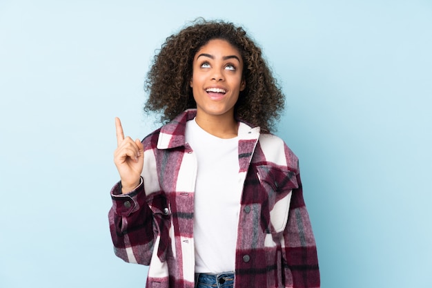 Jeune femme afro-américaine sur mur bleu pointant vers le haut et surpris