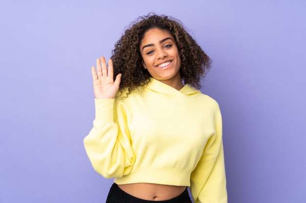 Jeune femme afro-américaine sur le mur saluant avec la main avec une expression heureuse