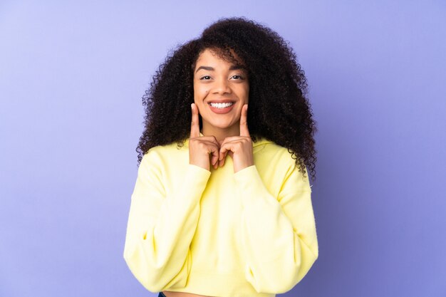 Jeune femme afro-américaine sur mur violet souriant avec une expression heureuse et agréable
