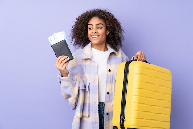 Jeune femme afro-américaine sur mur violet avec valise et passeport