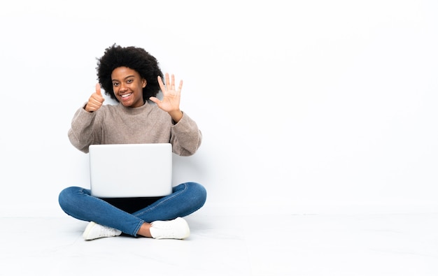 Jeune femme afro-américaine avec un ordinateur portable assis sur le sol en comptant six avec les doigts