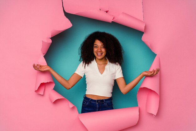 Jeune femme afro-américaine en papier déchiré isolé sur fond bleu montrant une expression de bienvenue.