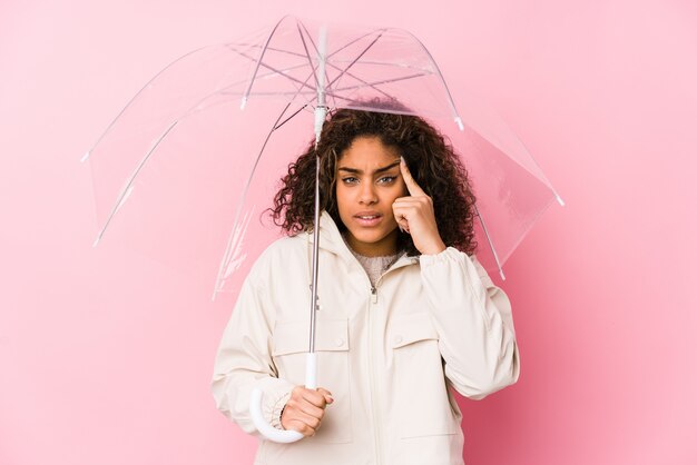 Jeune femme afro-américaine avec un parapluie montrant un geste de déception avec l'index.