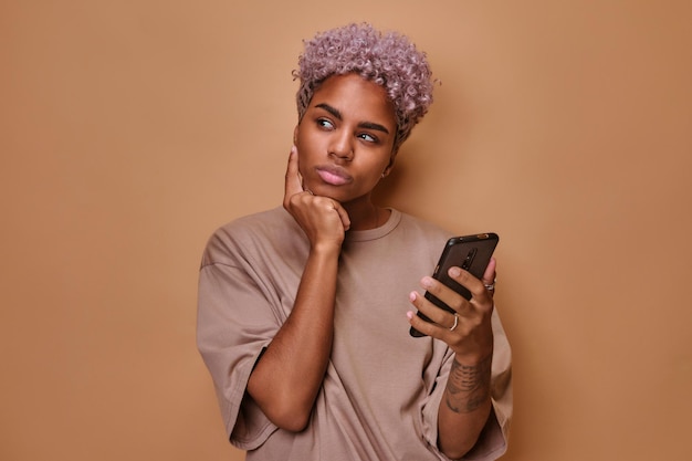 Une jeune femme afro-américaine pensive debout avec un téléphone utilise le chat en ligne