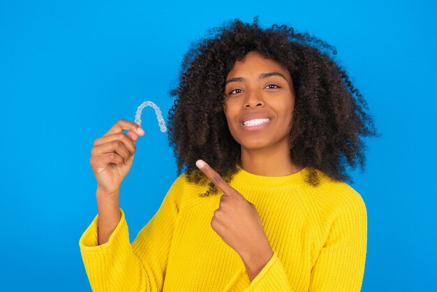 Jeune femme afro-américaine portant un pull jaune debout sur fond bleu