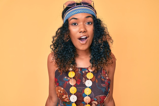 Jeune femme afro-américaine portant un style bohème et hippie effrayée et émerveillée par la bouche ouverte pour un visage surprise et incrédule