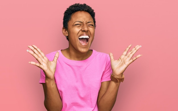 Jeune femme afro-américaine portant des vêtements décontractés célébrant la folie et la folie du succès avec les bras levés et les yeux fermés hurlant d'excitation. notion de gagnant