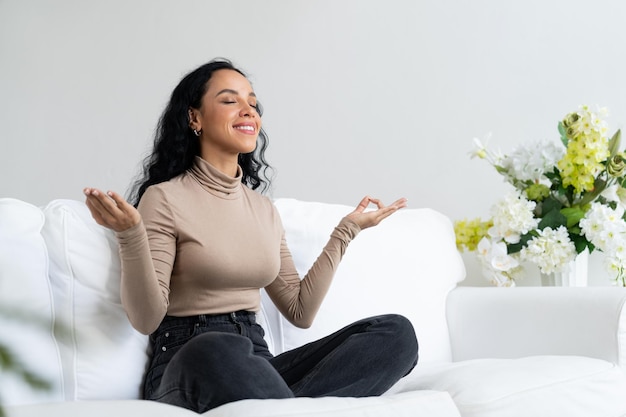 Une jeune femme afro-américaine pratique une méditation consciente cruciale à la maison dans le salon pour améliorer la santé mentale, la force et la vie paisible et belle.