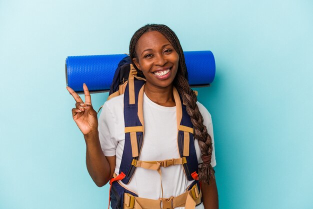 Jeune femme afro-américaine de randonnée isolée sur fond bleu joyeuse et insouciante montrant un symbole de paix avec les doigts.