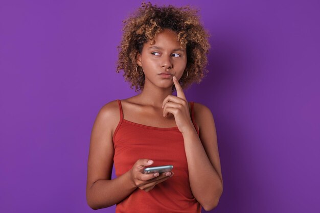 Photo une jeune femme afro-américaine réfléchie regarde sur le côté et tient un téléphone portable.