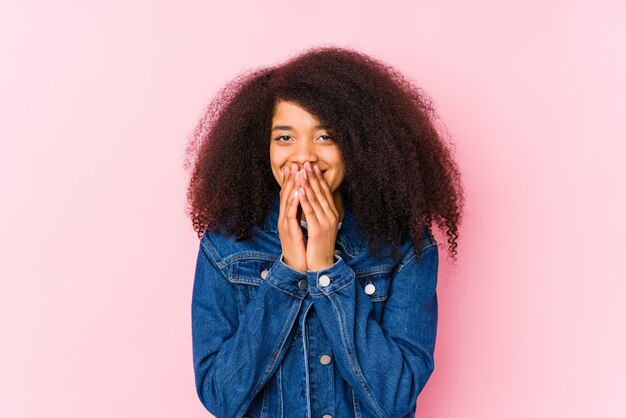 Jeune femme afro-américaine rire de quelque chose, couvrant la bouche avec les mains.