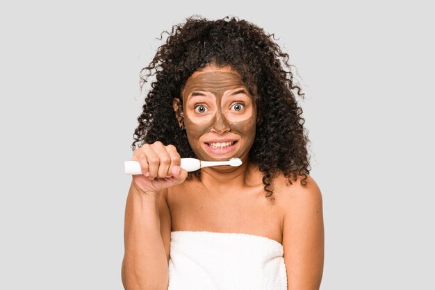 Jeune femme afro-américaine se brosser les dents et s'appliquant un masque facial isolé