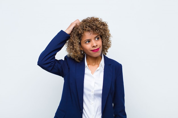 Jeune femme afro-américaine se sentant perplexe et confus, se grattant la tête et regardant sur le côté sur un mur plat