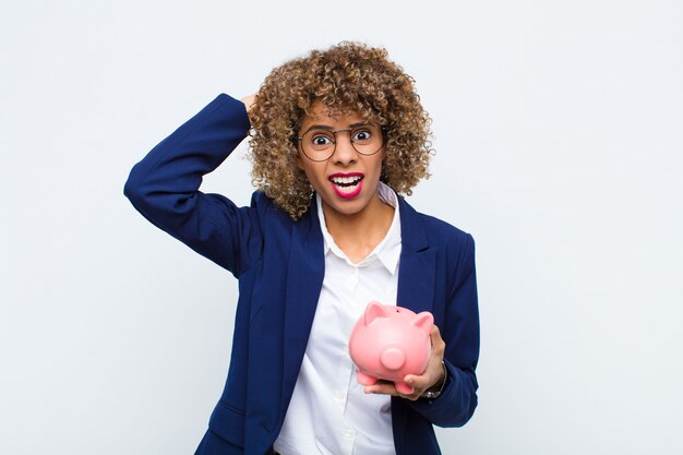 Jeune femme afro-américaine se sentant stressé, inquiet, anxieux ou effrayé, les mains sur la tête, paniquant par erreur avec une tirelire