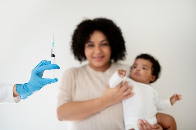 Photo une jeune femme afro-américaine souriante et aimante tenant un bébé dans ses bras regarde la main du médecin avec une seringue