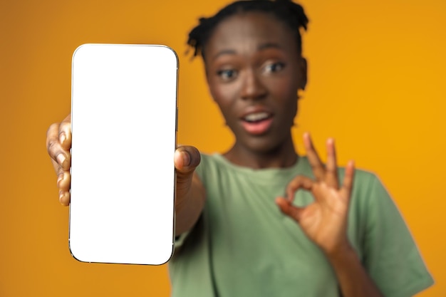 Jeune Femme Afro-américaine Souriante Montrant Un Smartphone Avec écran Blanc Sur Fond Jaune