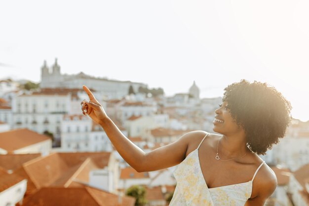 Une jeune femme afro-américaine souriante en robe pointe le doigt vers l'espace libre. Profitez de la promenade.