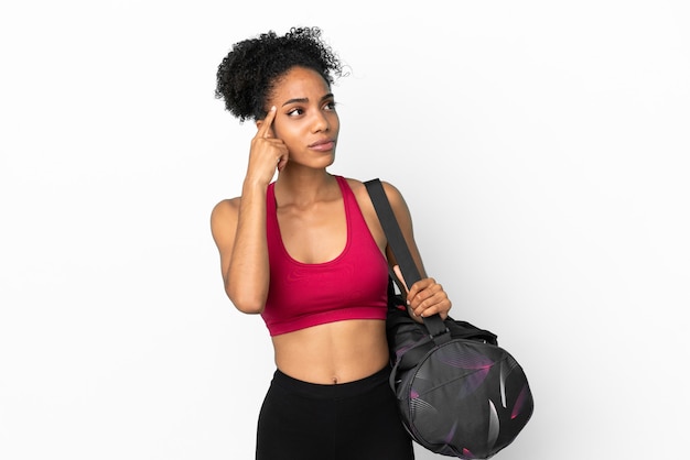 Jeune femme afro-américaine sportive avec sac de sport isolé sur fond bleu ayant des doutes et pensant