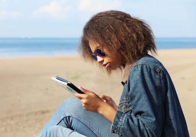 Jeune femme afro-américaine avec tablette sur la plage