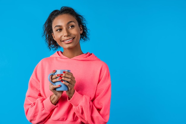 Jeune femme afro-américaine avec une tasse de café heureux de penser sur fond bleu isolé