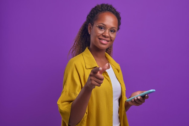 Jeune femme afro-américaine téléphone souriant et pointant le doigt à la caméra
