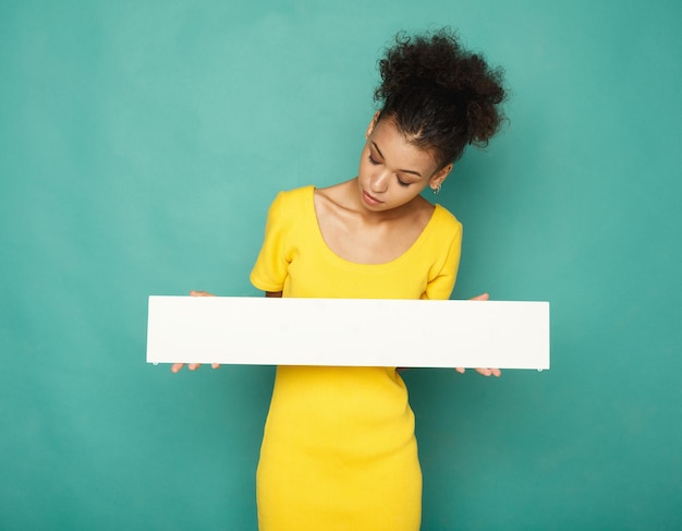 Jeune femme afro-américaine tenant une bannière blanche vierge avec espace de copie sur fond bleu