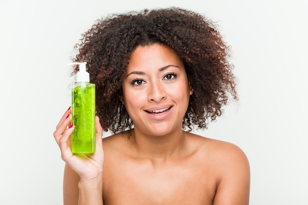 Jeune femme afro-américaine, tenant une bouteille d'aloe vera heureuse, souriante et gaie.