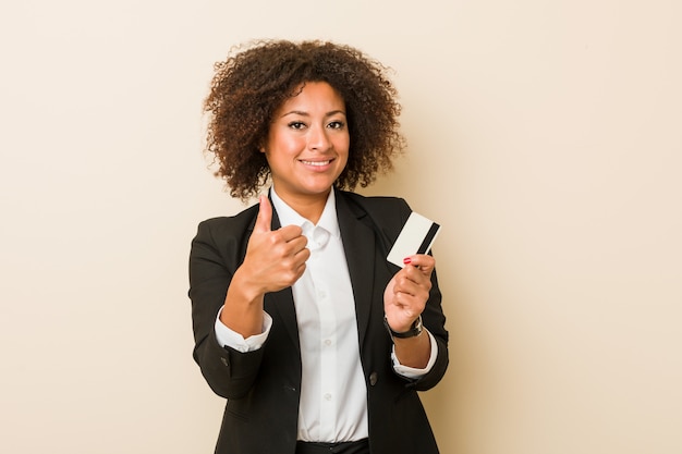 Jeune femme afro-américaine tenant une carte de crédit en souriant et en levant le pouce vers le haut