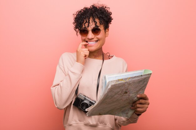 Jeune femme afro-américaine tenant une carte détendue en pensant à quelque chose en regardant un espace vide.