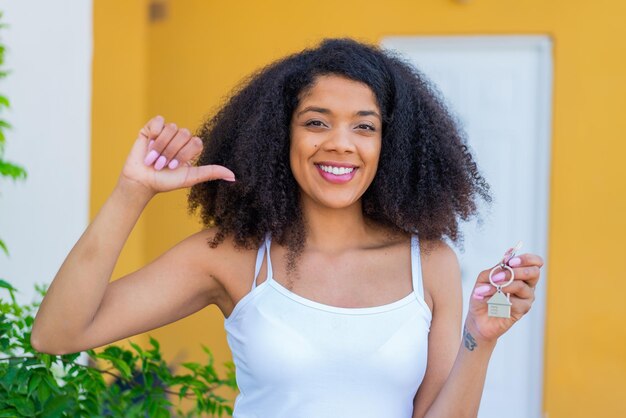 Une jeune femme afro-américaine tenant les clés de la maison à l'extérieur fière et satisfaite d'elle-même