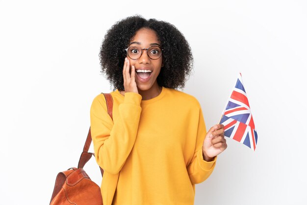 Jeune femme afro-américaine tenant un drapeau du Royaume-Uni isolé sur fond blanc avec une expression faciale surprise et choquée