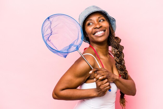 Jeune femme afro-américaine tenant un filet de pêche isolé sur fond rose