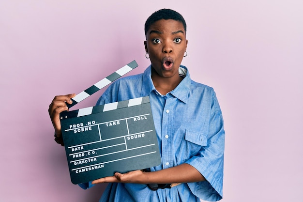 Jeune femme afro-américaine tenant un film vidéo à clin effrayé et choqué par la surprise et l'expression étonnée, la peur et le visage excité.