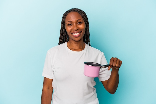 Jeune femme afro-américaine tenant pan isolé sur fond bleu heureux, souriant et joyeux.