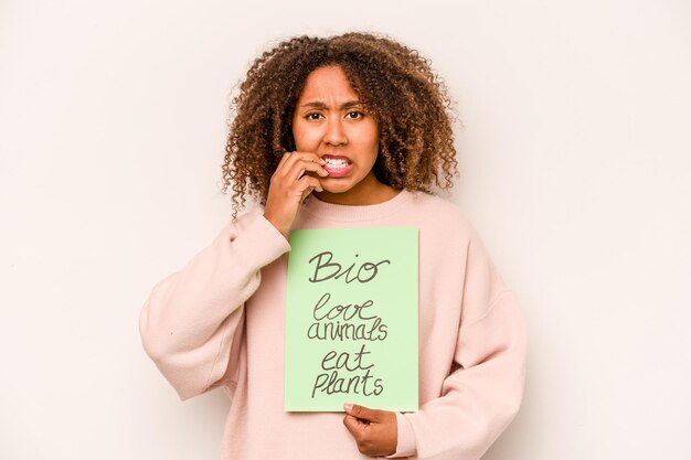 Jeune femme afro-américaine tenant une pancarte bio isolée sur fond blanc se rongeant les ongles nerveux et très anxieux
