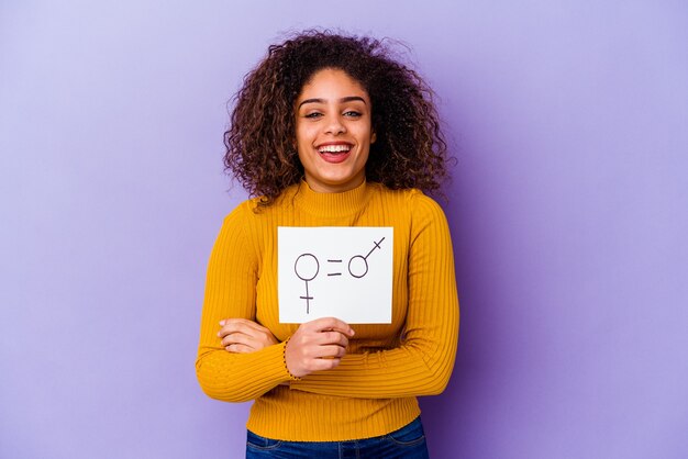 Jeune Femme Afro-américaine Tenant Une Pancarte D'égalité Des Sexes Isolée Sur Violet Rire Et S'amuser.