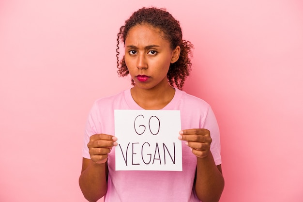 Jeune femme afro-américaine tenant une pancarte go vegan isolée sur fond rose