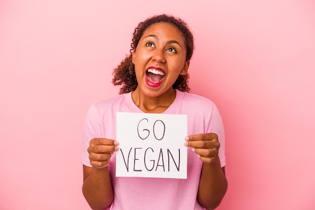 Jeune femme afro-américaine tenant une pancarte go vegan isolée sur fond rose