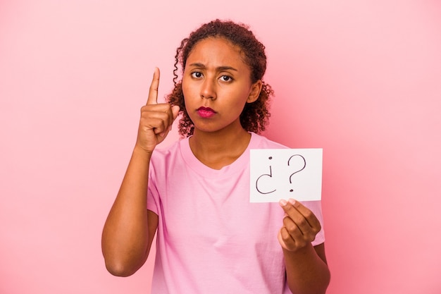 Jeune femme afro-américaine tenant une pancarte de question isolée sur fond rose