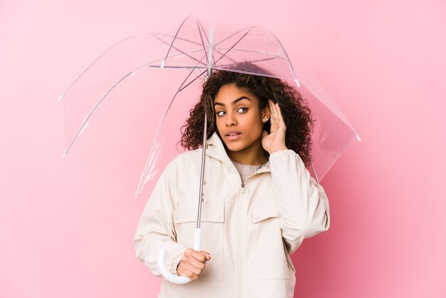 Jeune femme afro-américaine tenant un parapluie essayant d'écouter un potin.