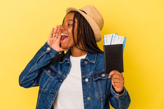 Jeune femme afro-américaine tenant un passeport isolé sur fond jaune criant et tenant la paume près de la bouche ouverte.