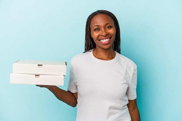 Jeune femme afro-américaine tenant des pizzas isolées sur fond bleu heureuse, souriante et joyeuse.